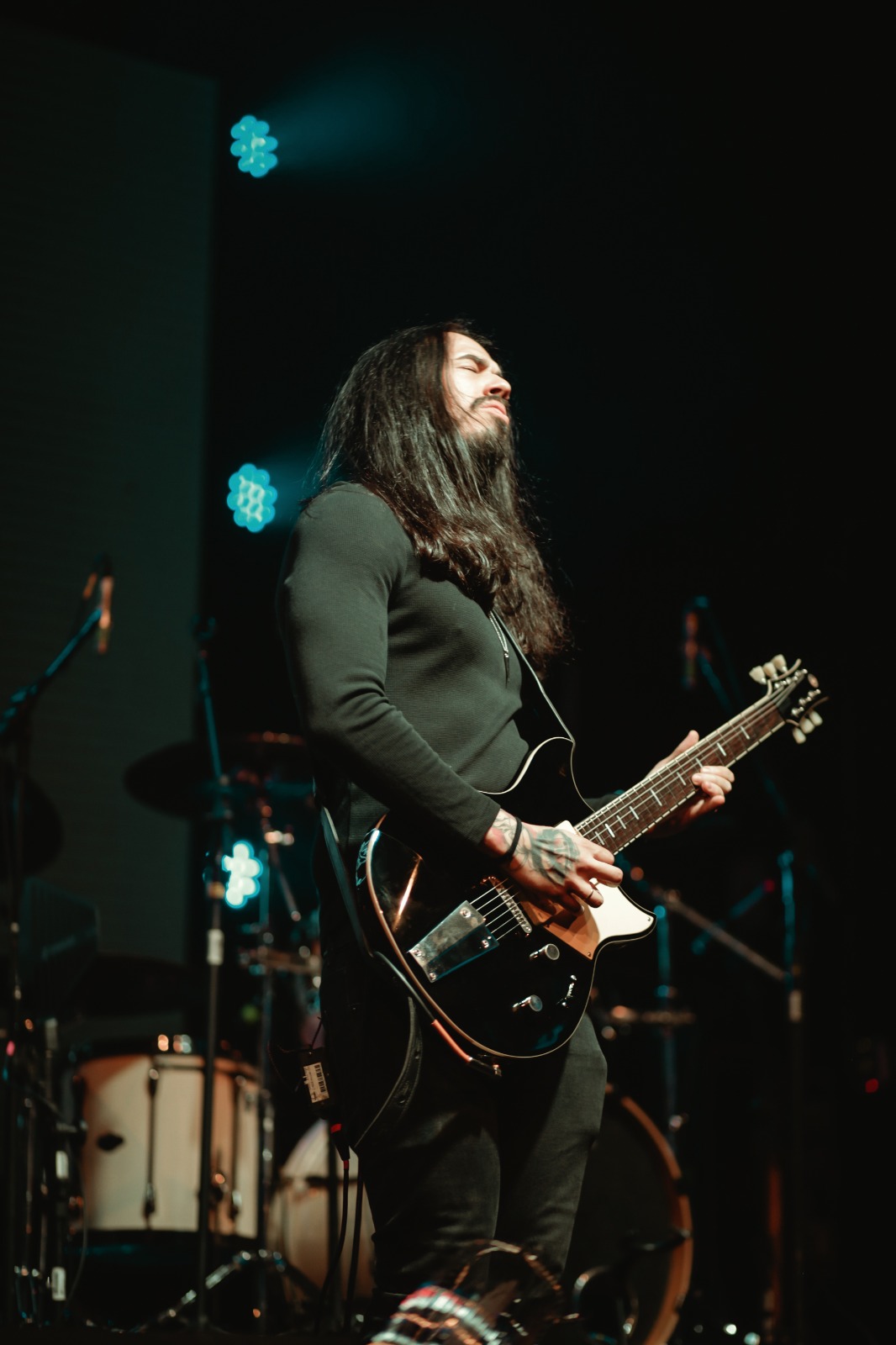 Gui Beltrame tocando guitarra em apresentação ao vivo, com iluminação de palco